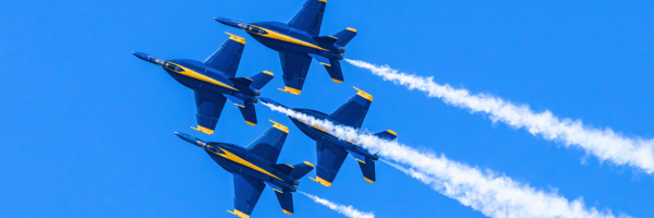 Four blue and yellow jets flying in formation against a clear blue sky, trailing white smoke.
